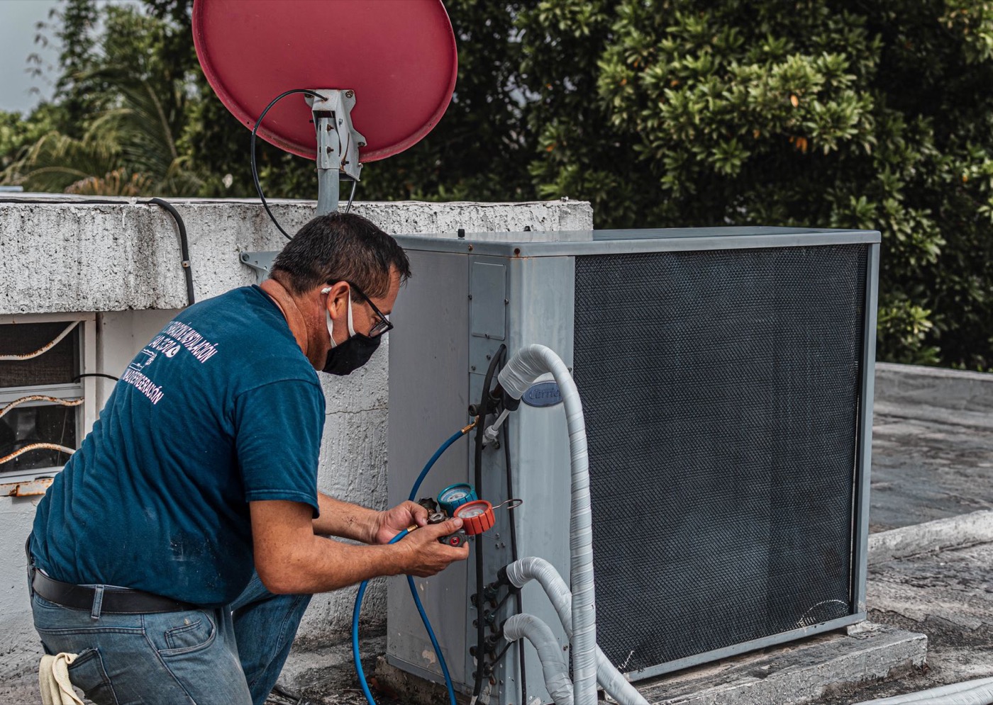 A technician reading a manifold gauge connected to an outdoor air conditioning unit